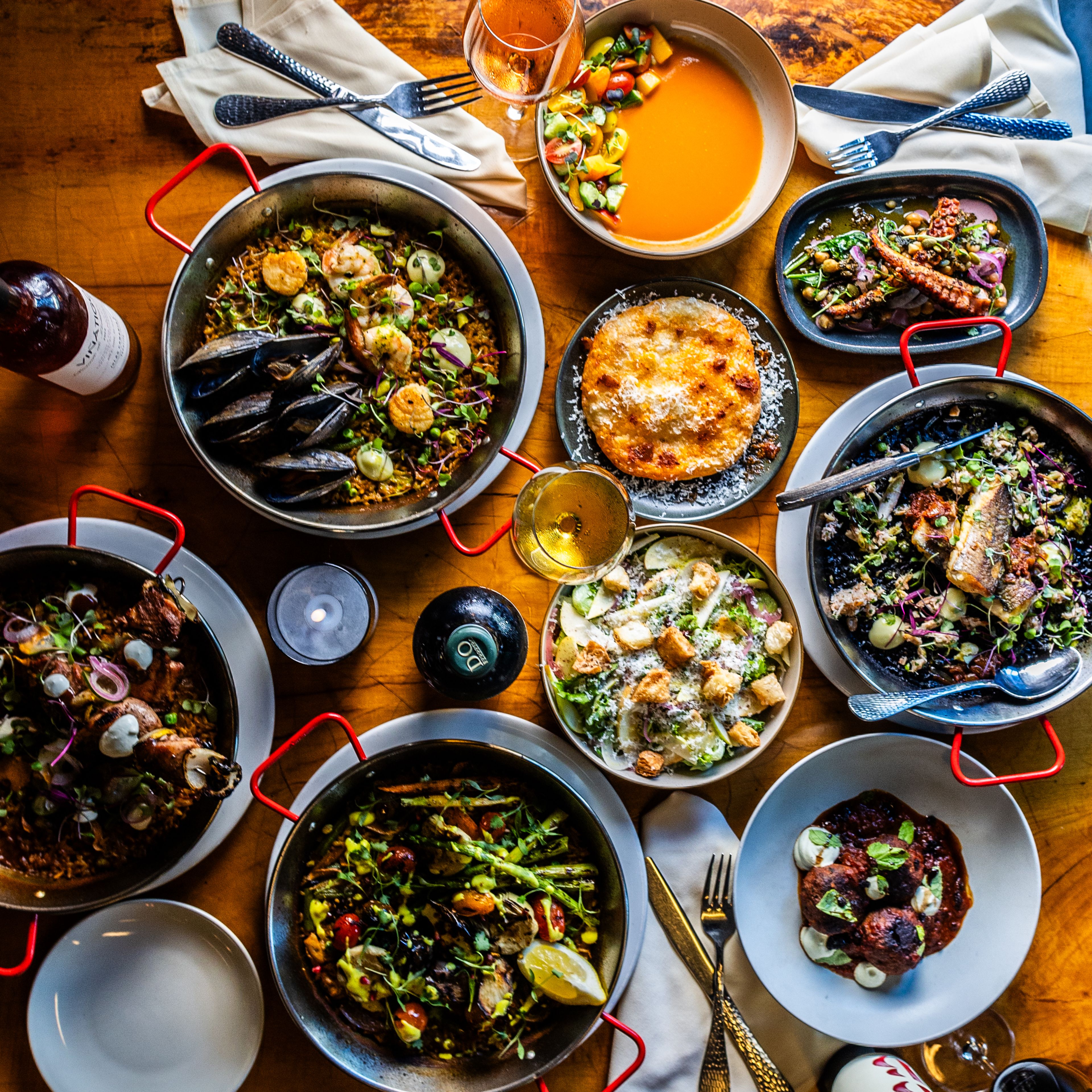 Multiple pans of paella with sides dishes and drinks