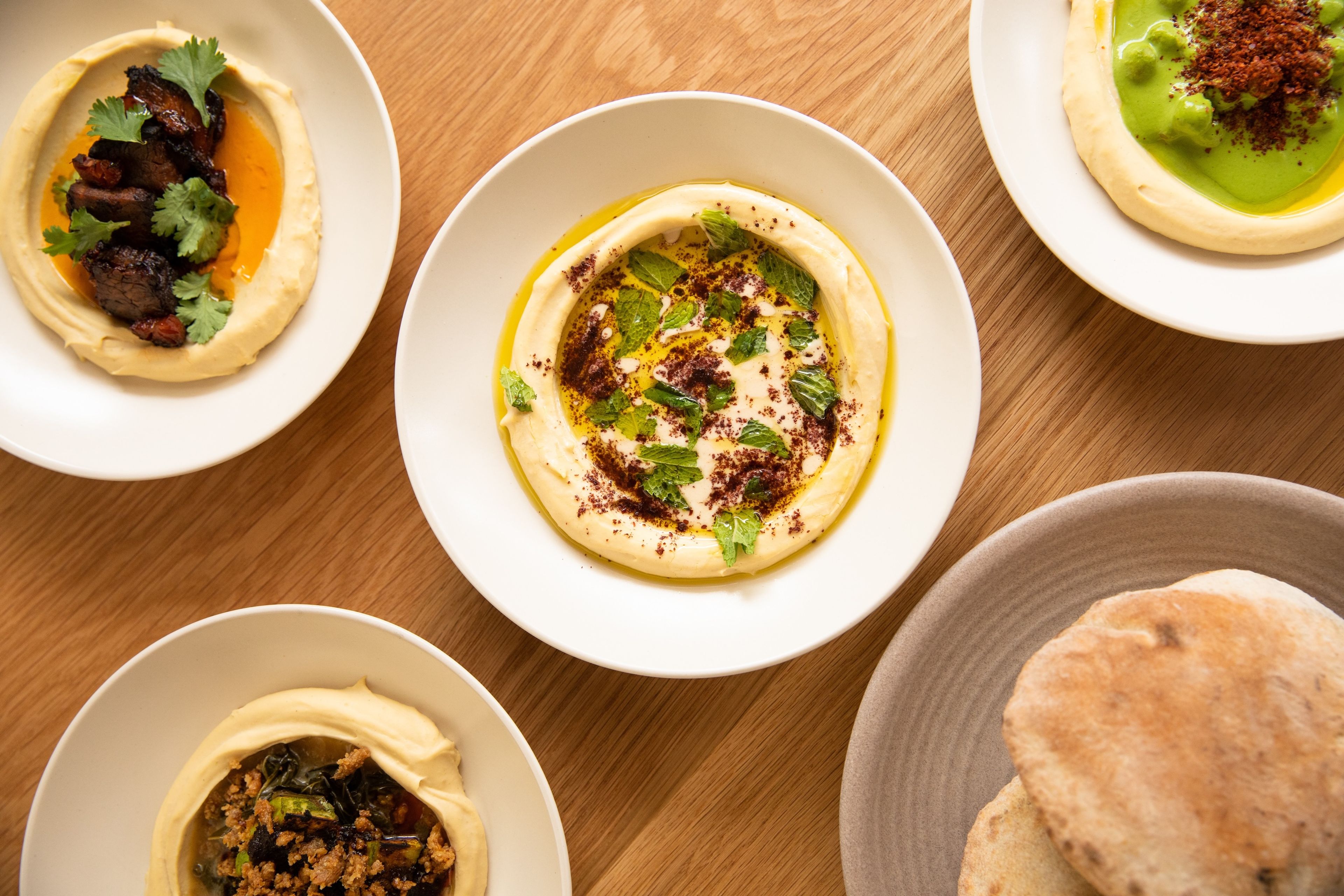 Multiple hummuses with a plate of pita on a wooden table