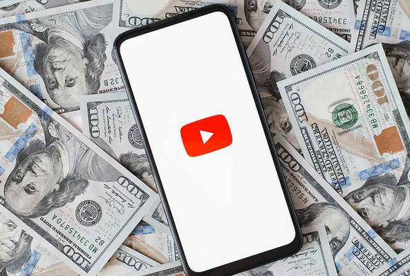 Smartphone displaying YouTube logo on screen over scattered hundred dollar bills background