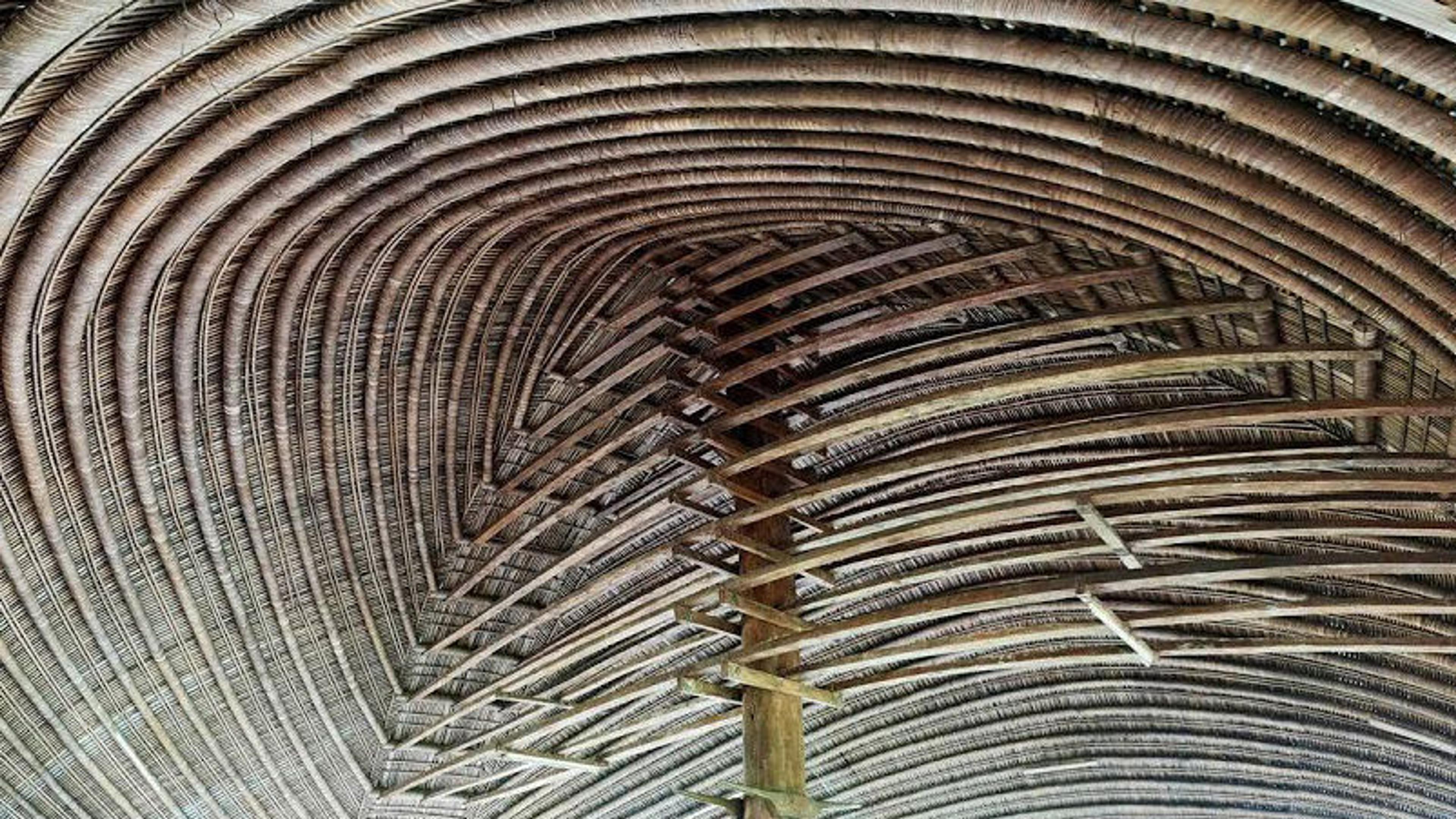 Curved bamboo ceiling with intricate, layered patterns, supported by a central wooden beam. The design is symmetrical and organic, evoking nature.