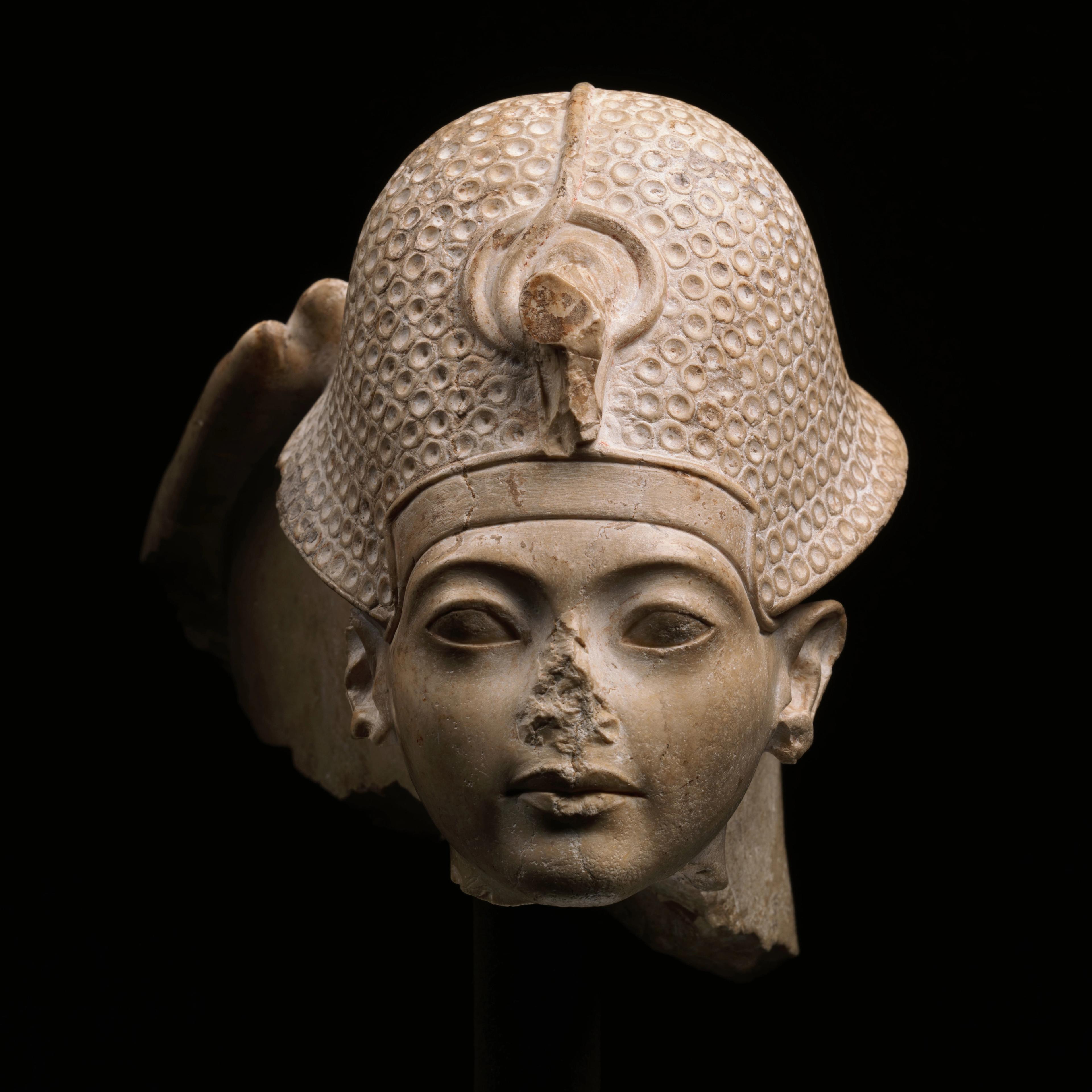 A detailed stone sculpture of a head wearing a textured helmet and missing a nose.