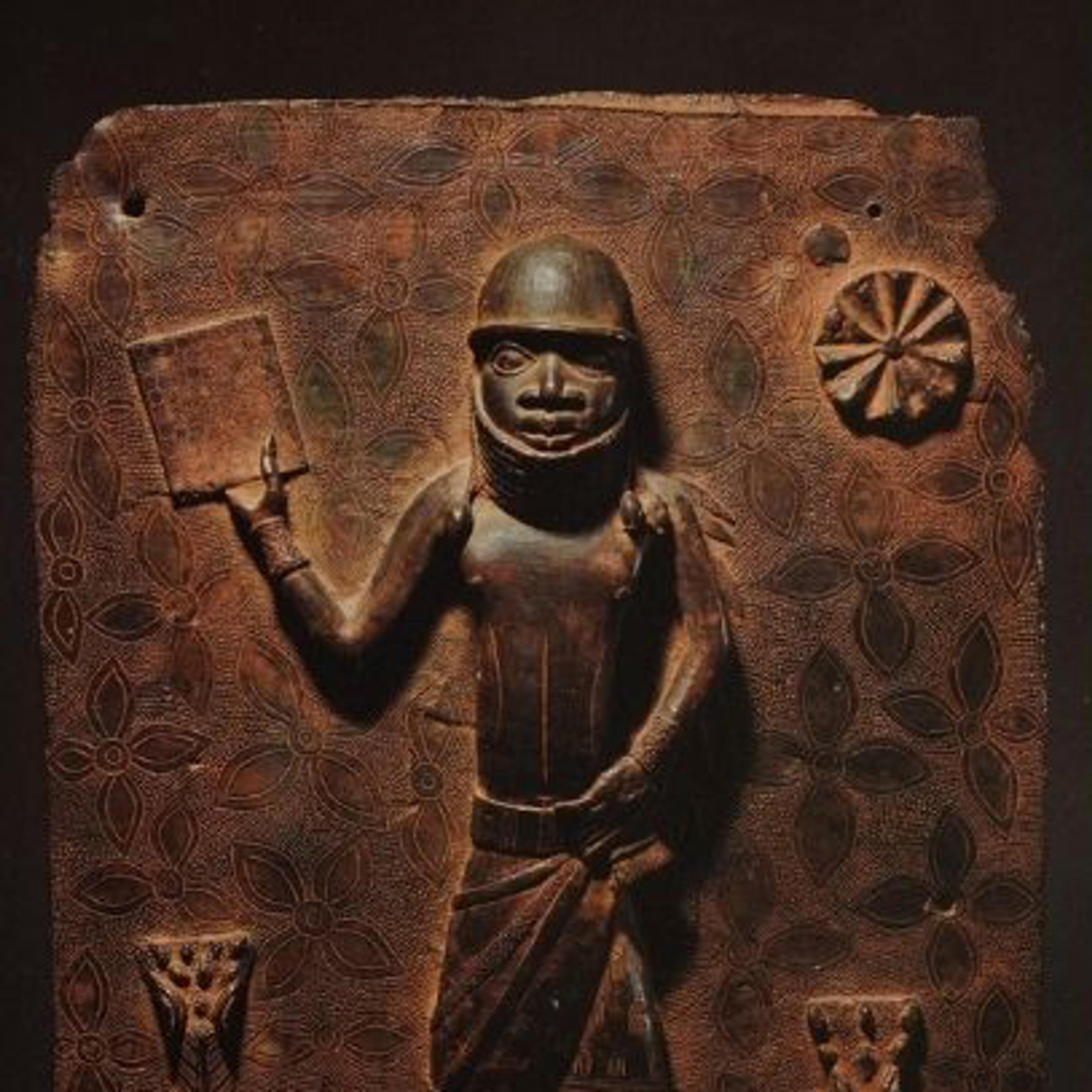 Bronze Benin sculpture with a figure holding a book. The background is adorned with floral motifs