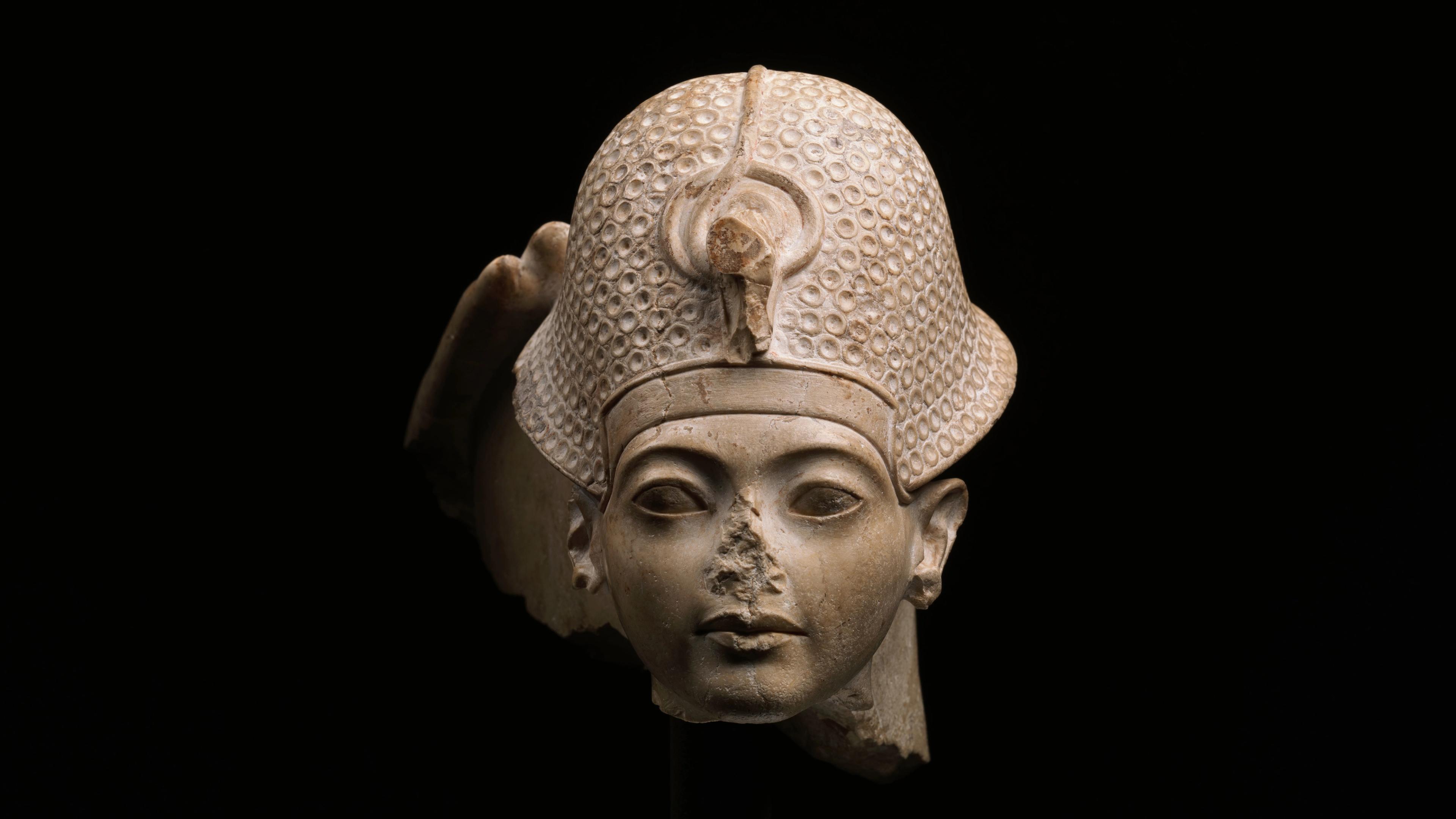 A detailed stone sculpture of a head wearing a textured helmet and missing a nose.