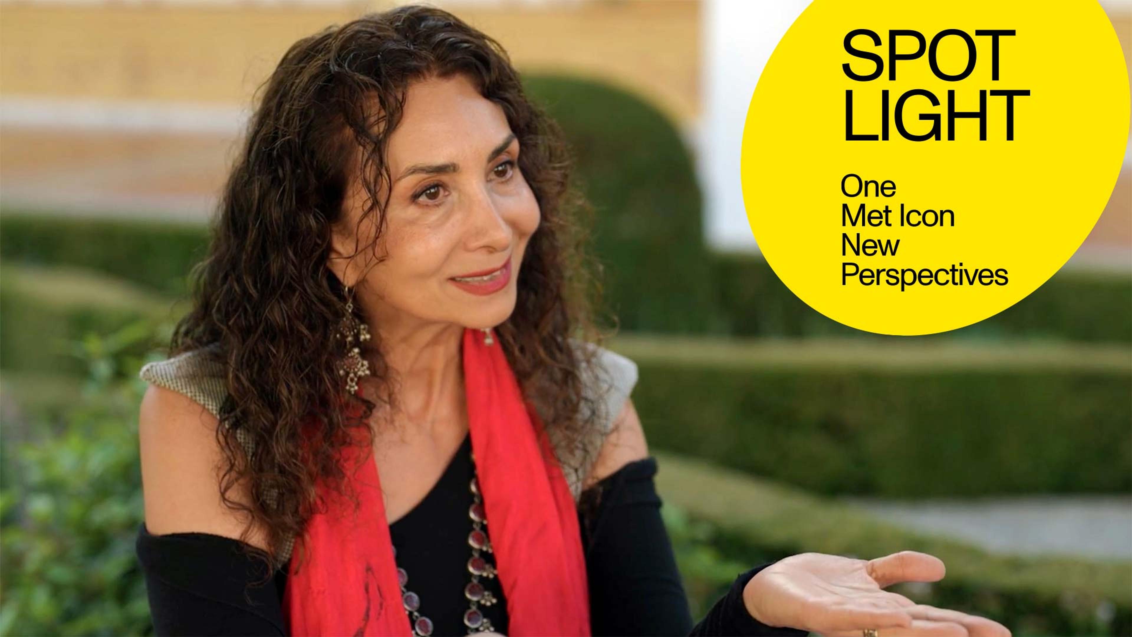 Artist Sholeh Wolpé seated in a garden wearing a black shirt and red scarf