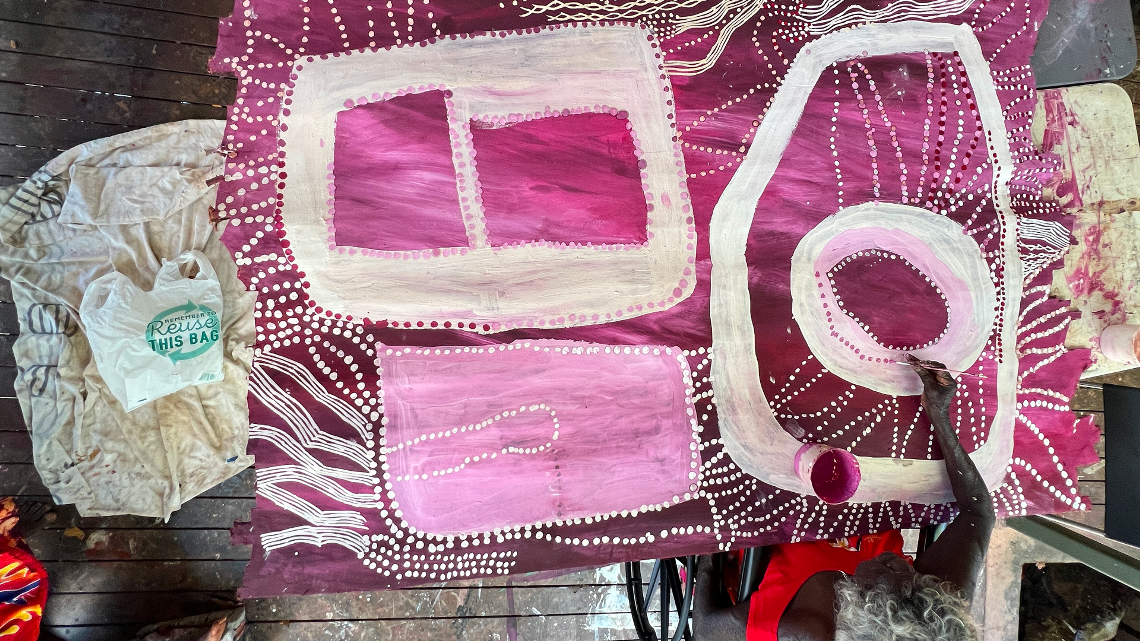 Woman painting pink and white designs on a large piece of bark