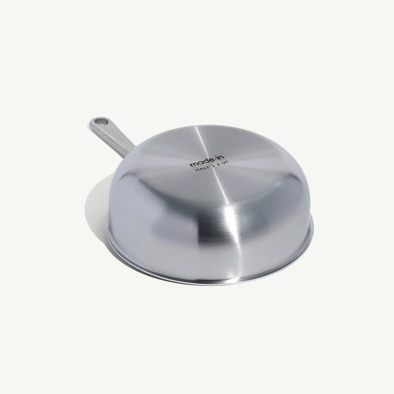 A stainless steel frying pan rests upside-down on a white surface, reflecting light off its curved, shiny exterior.