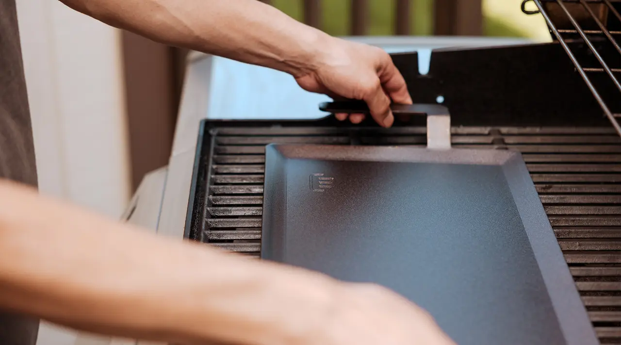 A person is opening or closing a barbecue grill with a focus on their hand on the handle.