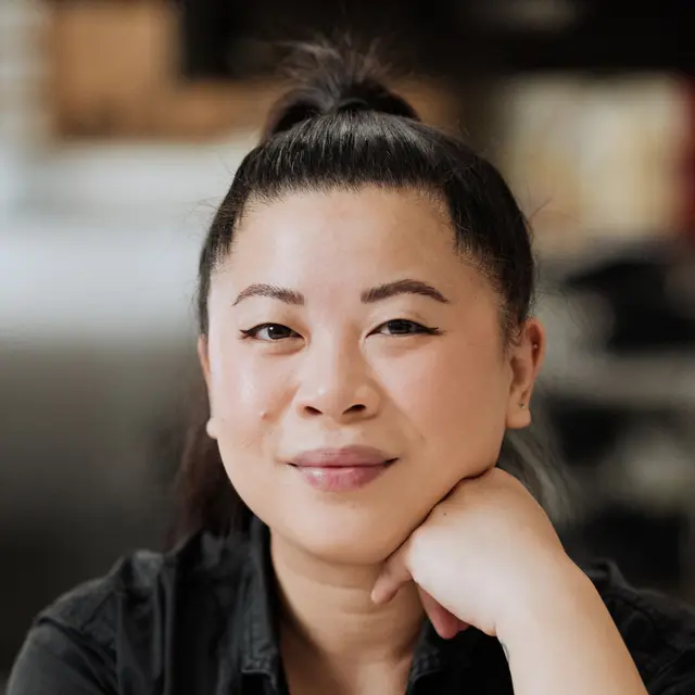A portrait of a smiling woman with her hand on her chin and a topknot hairstyle.