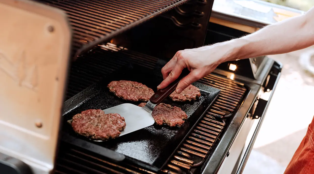 A person is grilling hamburgers on an outdoor barbecue.