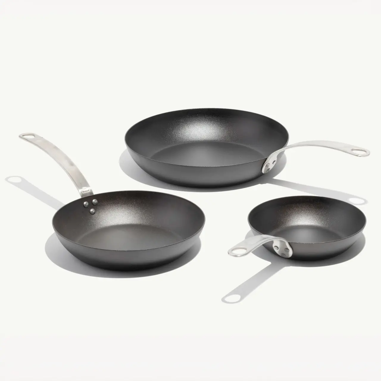 Three different-sized frying pans with metal handles are arranged on a white background.