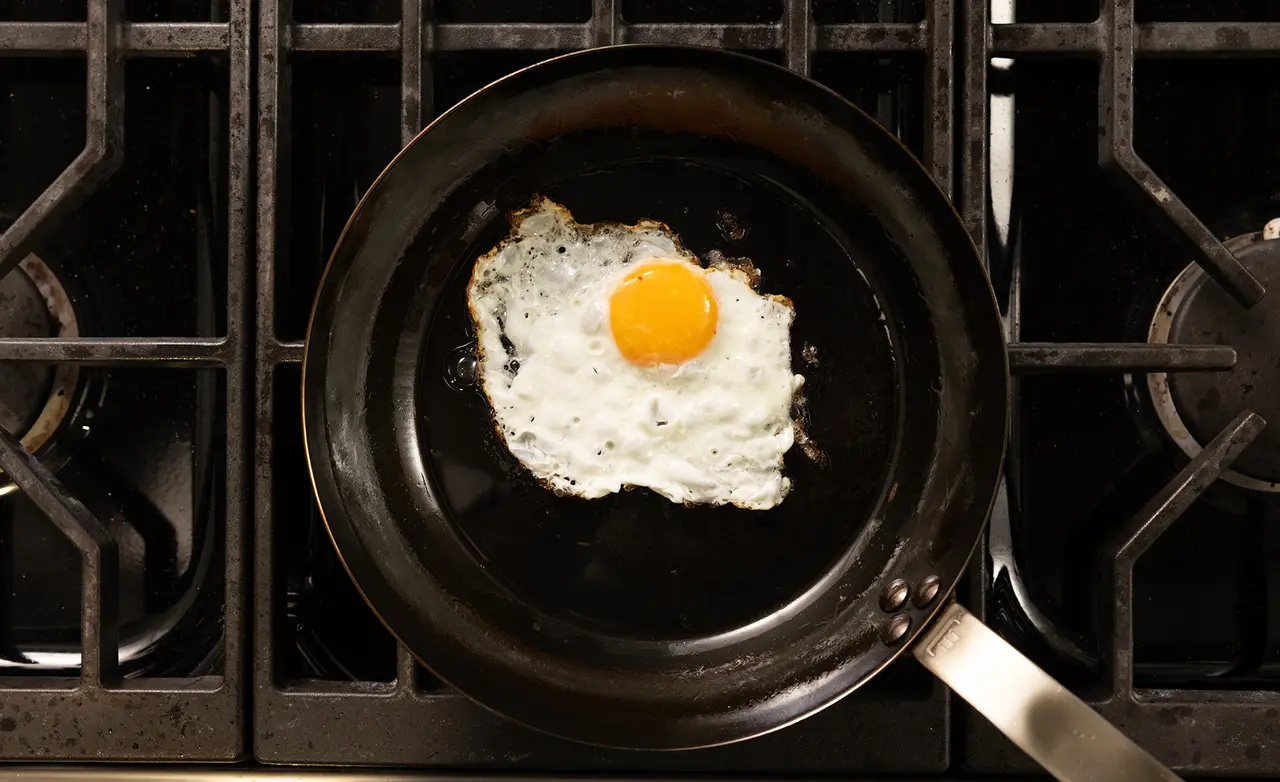 A fried egg with a bright yellow yolk is cooking in a black frying pan on a stovetop.