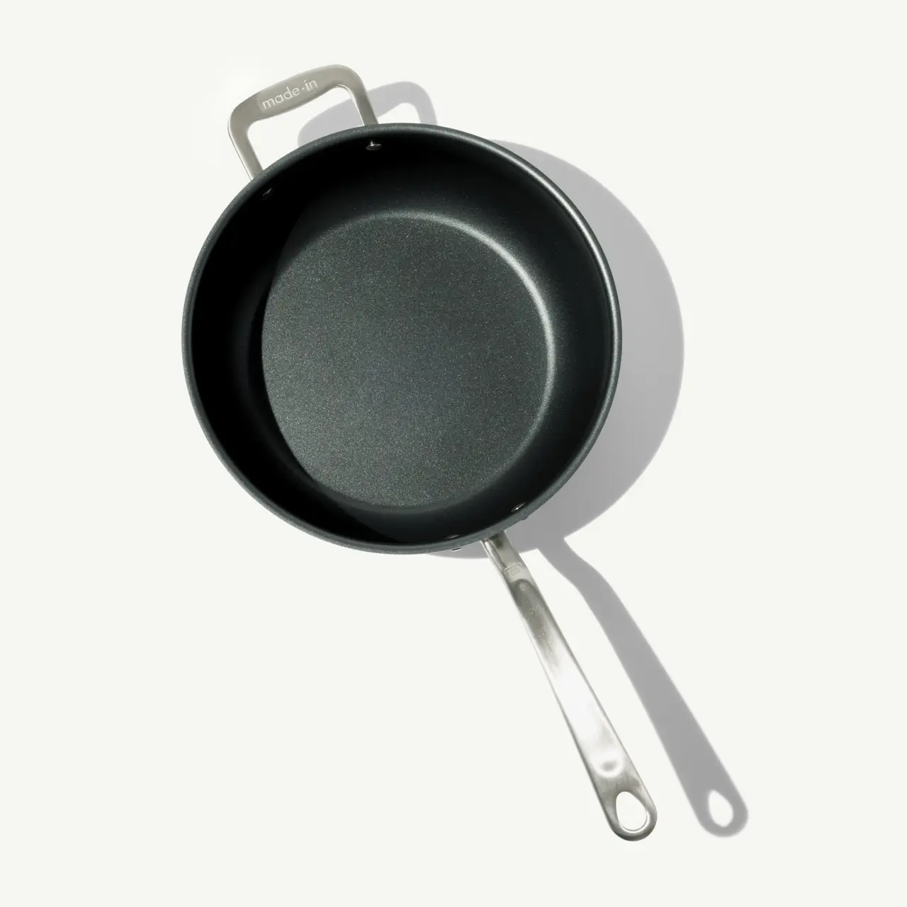 A round, non-stick frying pan with a stainless steel handle, casting a shadow on a light background.