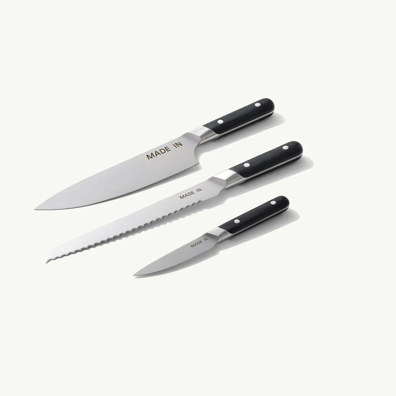 Three kitchen knives with black handles, featuring a chef's knife, a serrated knife, and a paring knife, all labeled "MADE IN."