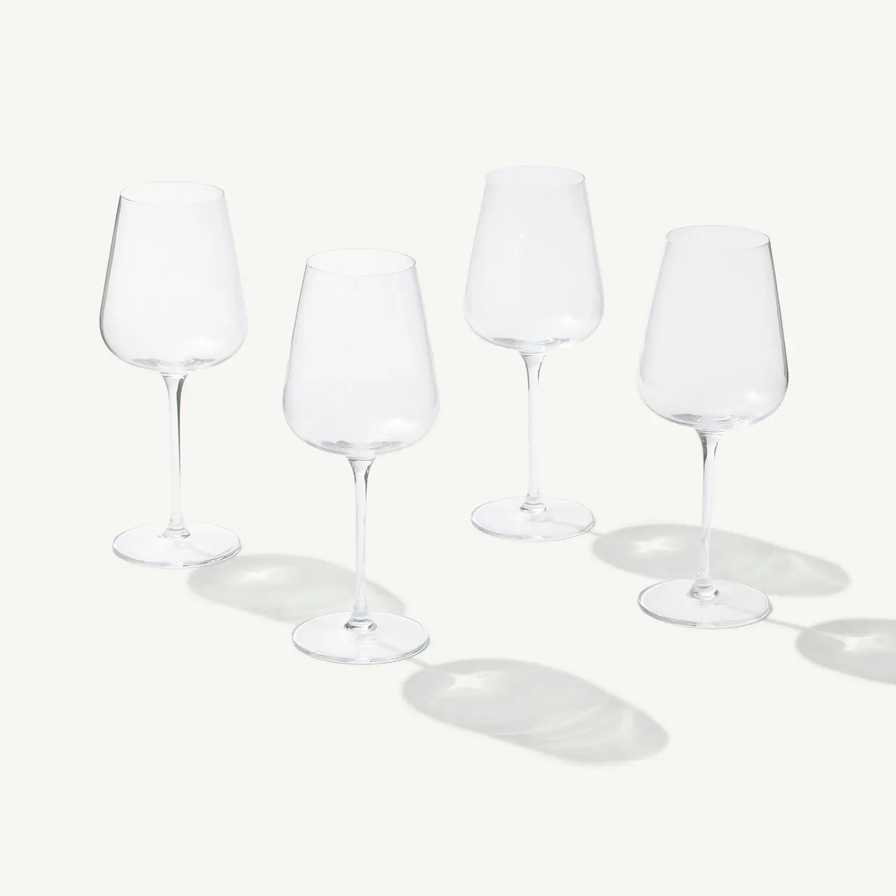 Four empty wine glasses with long stems are arranged on a white surface casting soft shadows.