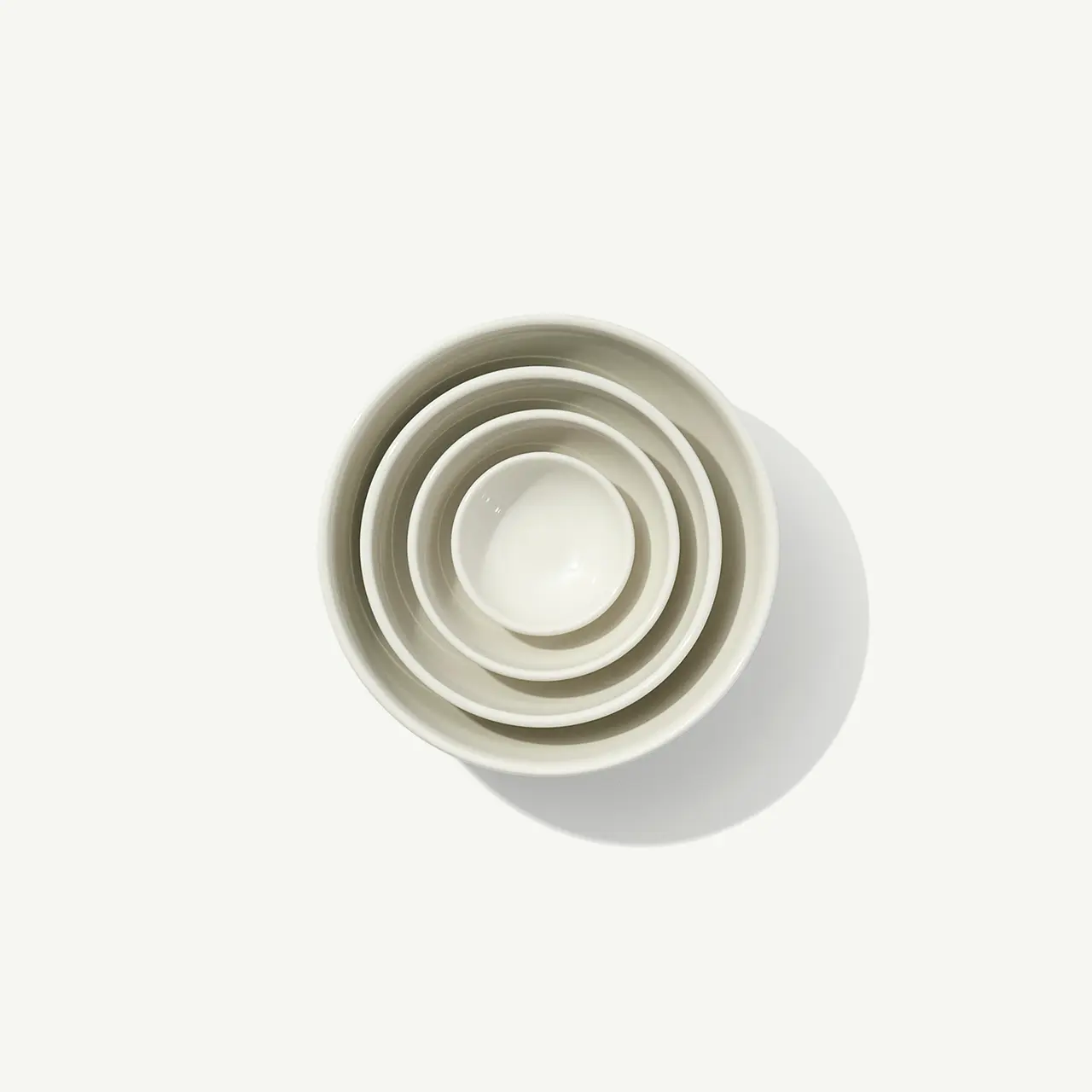 Four nested white bowls of varying sizes are arranged concentrically against a plain background.