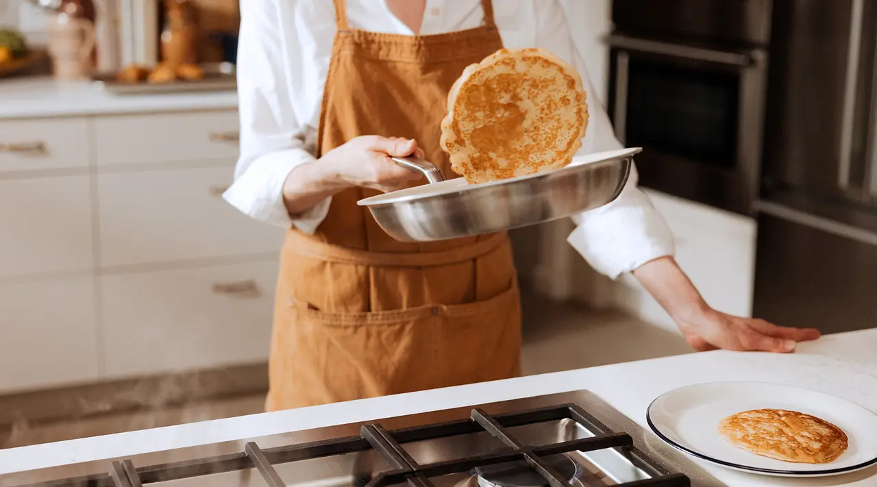 A person in a brown apron is skillfully flipping a pancake in a kitchen setting.