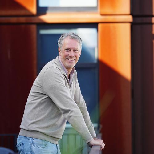 a man is leaning on a railing in front of a building and smiling .
