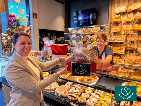 a woman is holding a bag of bread in a bakery .