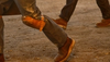 Two construction workers in work boots and tool belts walk on a dusty site.