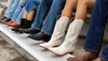 Several people sitting side by side on benches, showing a variety of boots including cowboy boots, black leather boots, and brown leather shoes.