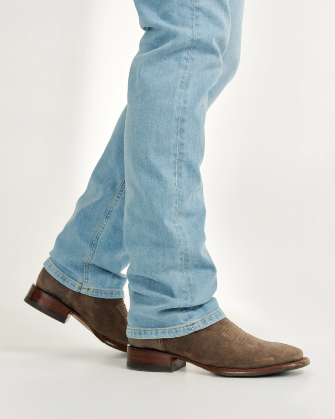 Person wearing light blue jeans and brown cowboy boots, walking with feet crossing over one another.