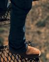 Person wearing jeans and brown shoes stands on an outdoor metal grate platform, overlooking a blurred landscape below.